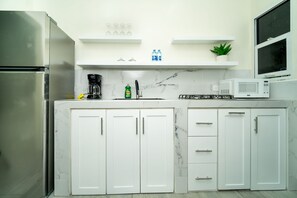 A modern kitchen with white cabinets, a stainless steel refrigerator, a microwave, and a coffee maker.