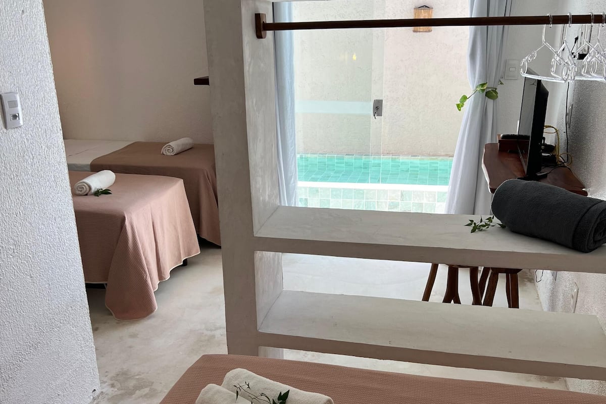 Un cuarto de spa con dos camillas de masaje, una ventana que da a una piscina y un banco de madera con toallas.
