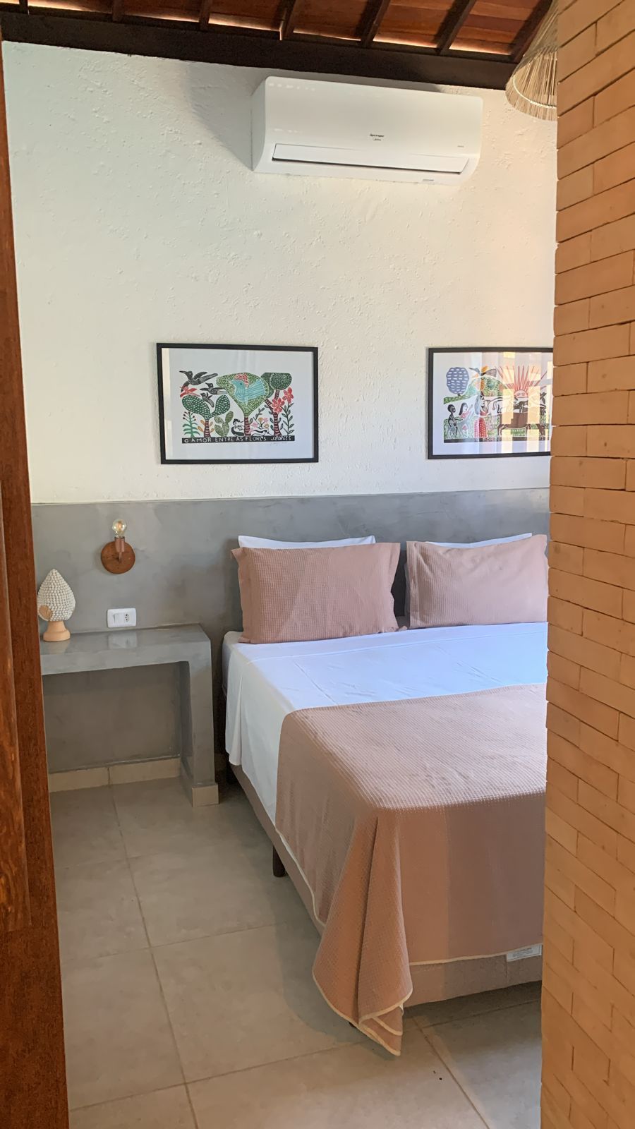 Un dormitorio con una cama, dos mesitas de noche, un aire acondicionado y dos cuadros enmarcados en la pared.