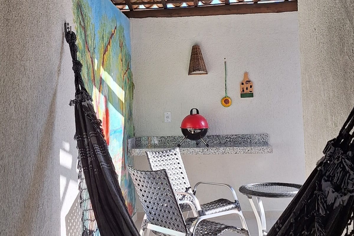 Una hamaca bajo una pérgola de madera, un mural en la pared y una zona de barbacoa con sillas.
