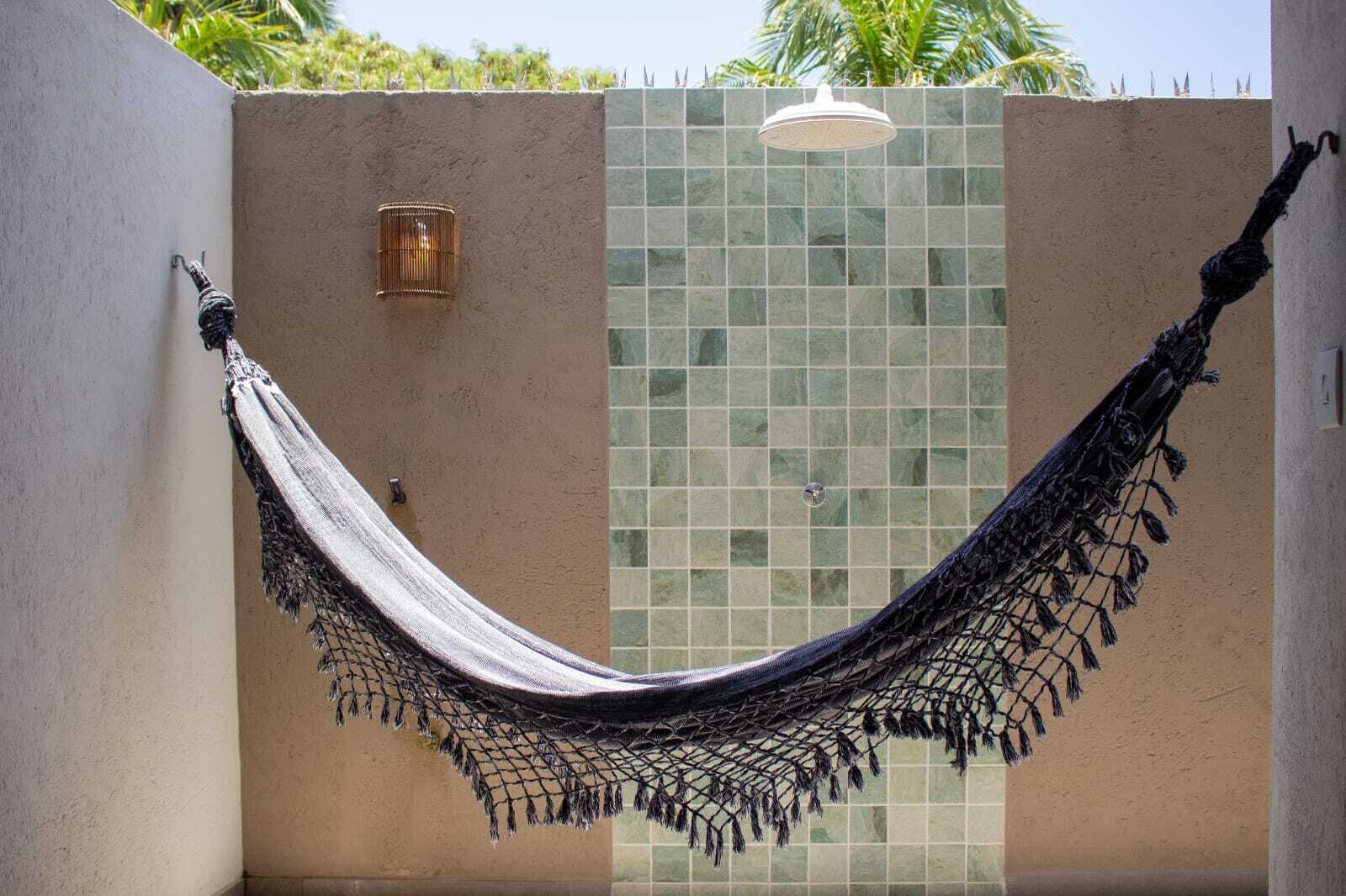 A hammock hanging between two walls with a tiled wall and a plain wall, a small light fixture, and a ceiling-mounted light.