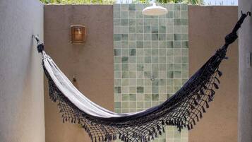 A hammock hanging between two walls with a tiled wall and a plain wall, a small light fixture, and a ceiling-mounted light.