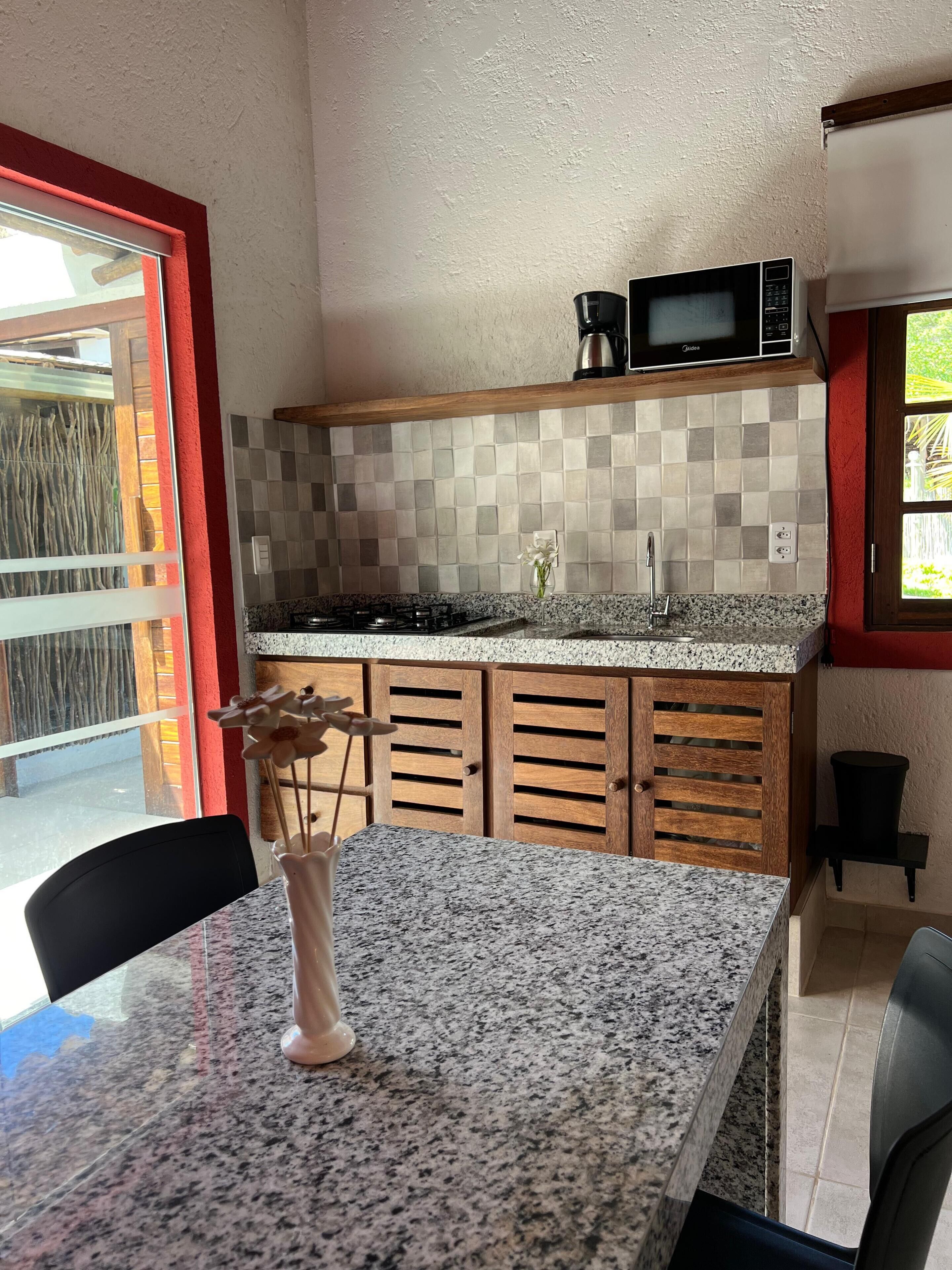 A kitchen with a granite countertop, wooden cabinets, a microwave, and a vase with flowers on the table.