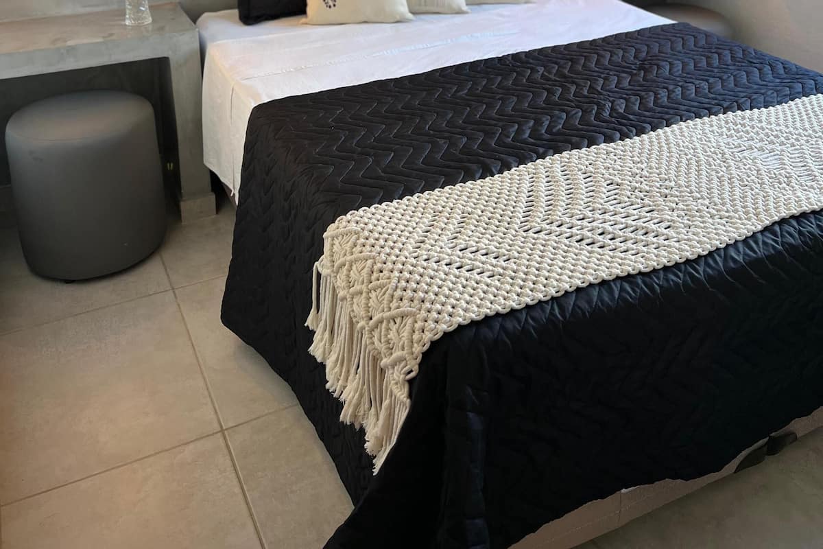 Un dormitorio moderno con una cama grande, dos mesitas de noche, un taburete redondo y dos lámparas de pared.