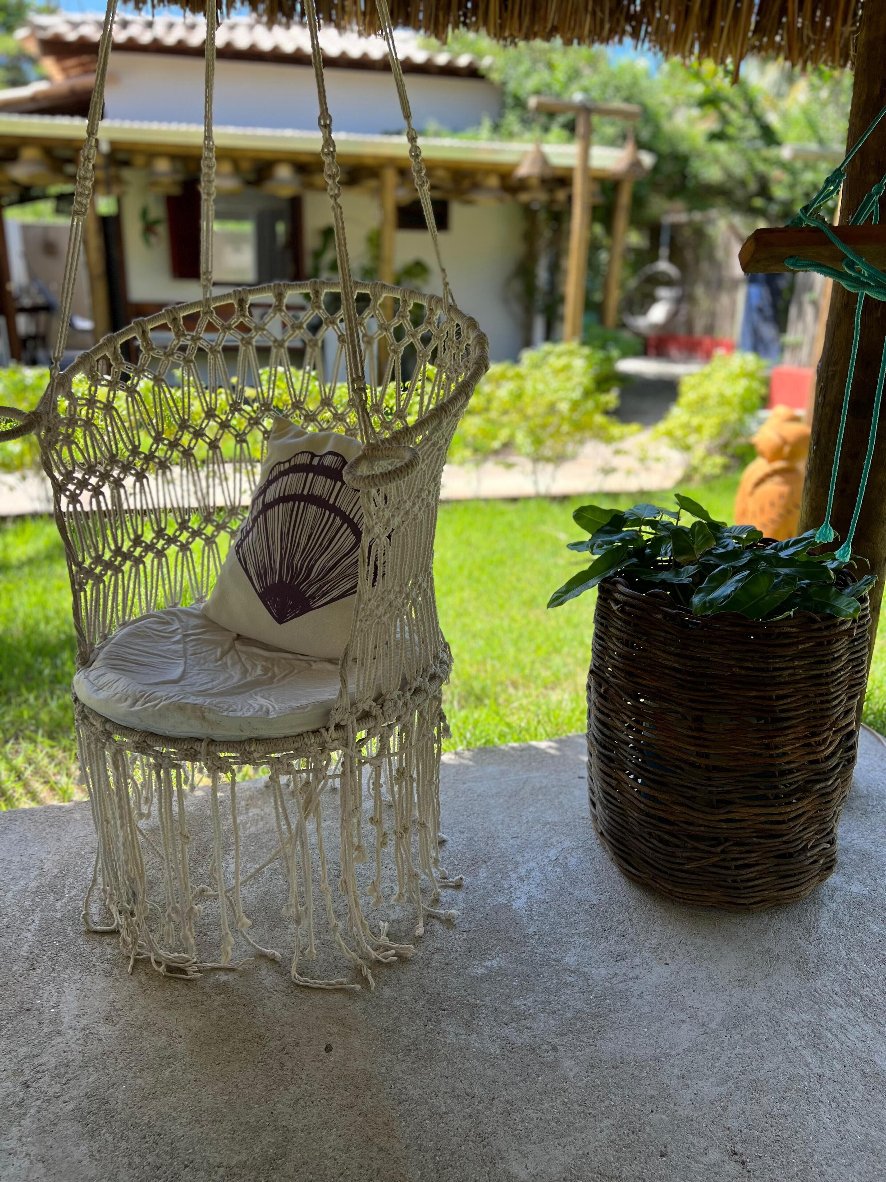 Une chaise en macramé avec un coussin et une plante en pot placée à côté.