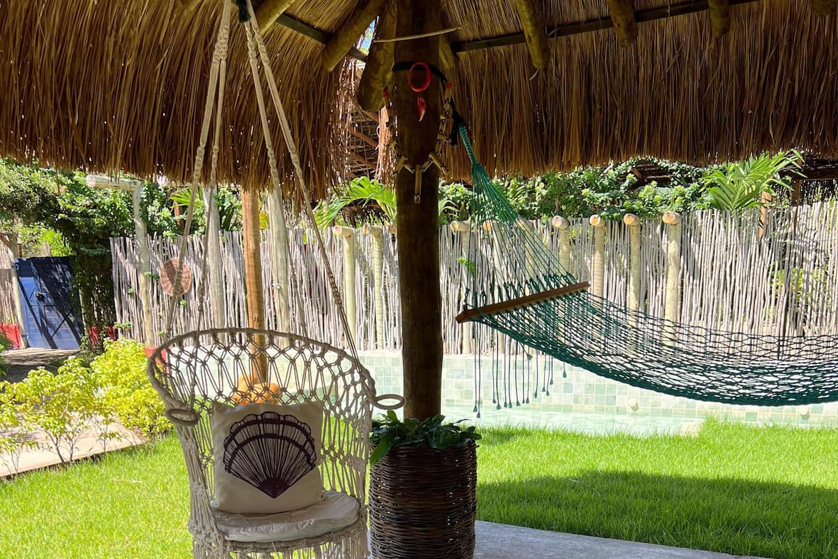 Una hamaca, una silla de mimbre y un espacio de descanso acolchado bajo un techo de paja.