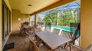 An outdoor patio with a pool, wooden furniture, and a covered seating area. - 9BR Home w/ Private Pool, Game Room, & Free Resort Access (Kissimmee)