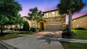 A residential property with a stone facade, a garage, and a well-maintained lawn with palm trees. - 9BR Home w/ Private Pool, Game Room, & Free Resort Access (Kissimmee)