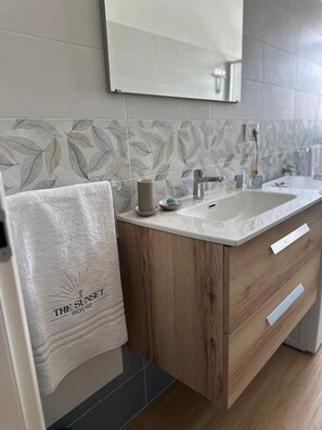 A modern bathroom with a wooden vanity, a large mirror, and a towel with "The Sunset House" logo. - Live the Cilento! Rent your apartment in Santa Maria di Castellabate (Campania)