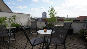 A rooftop terrace with outdoor seating, including round tables and chairs, surrounded by potted plants and a view of a cityscape. - Hotel Ambert (Berlin)