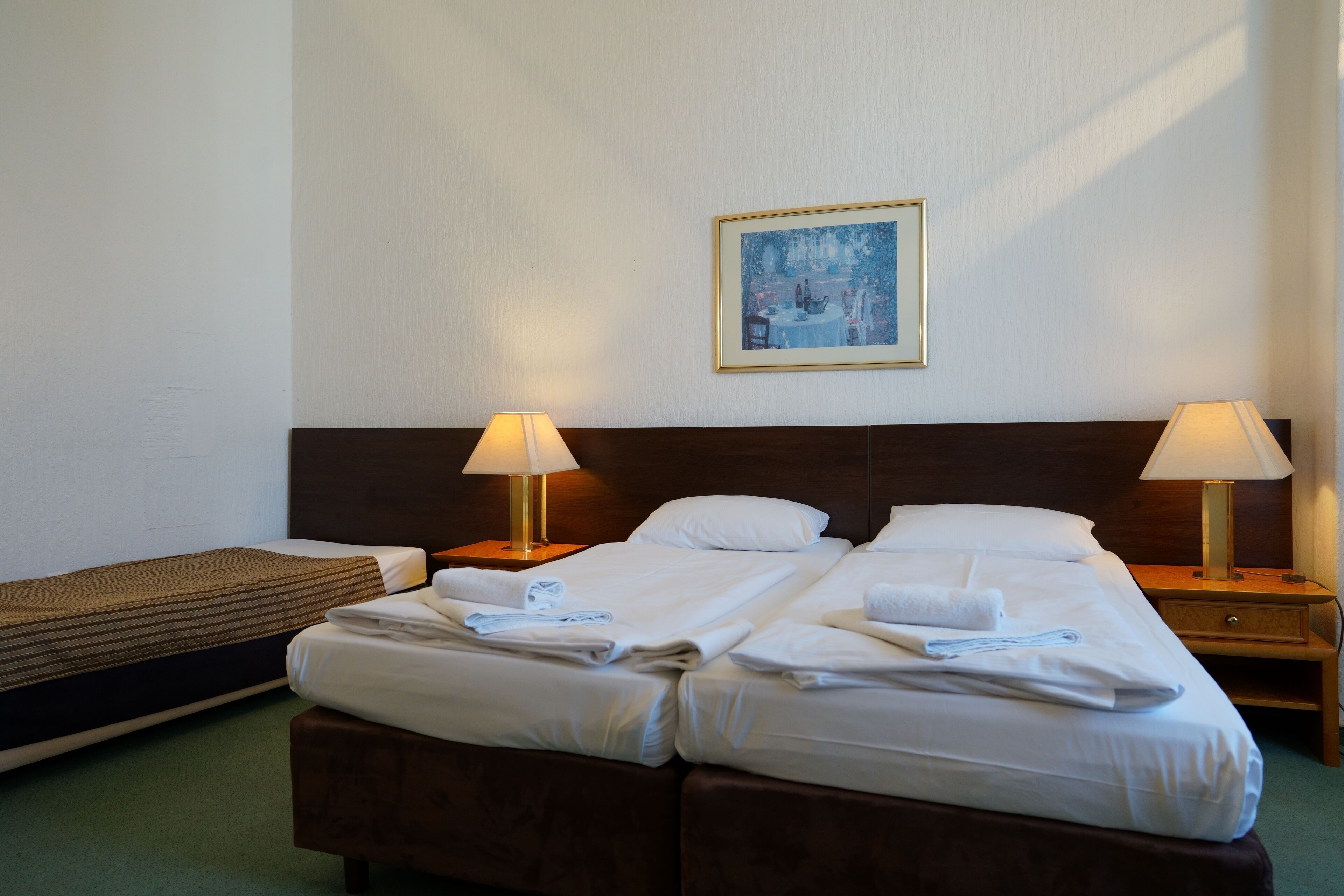 A hotel room with two beds, a small table, two bedside lamps, and a painting on the wall.