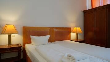 Una habitación de hotel con una cama bien hecha, dos lámparas de noche, un cabecero de madera y un armario de madera.
