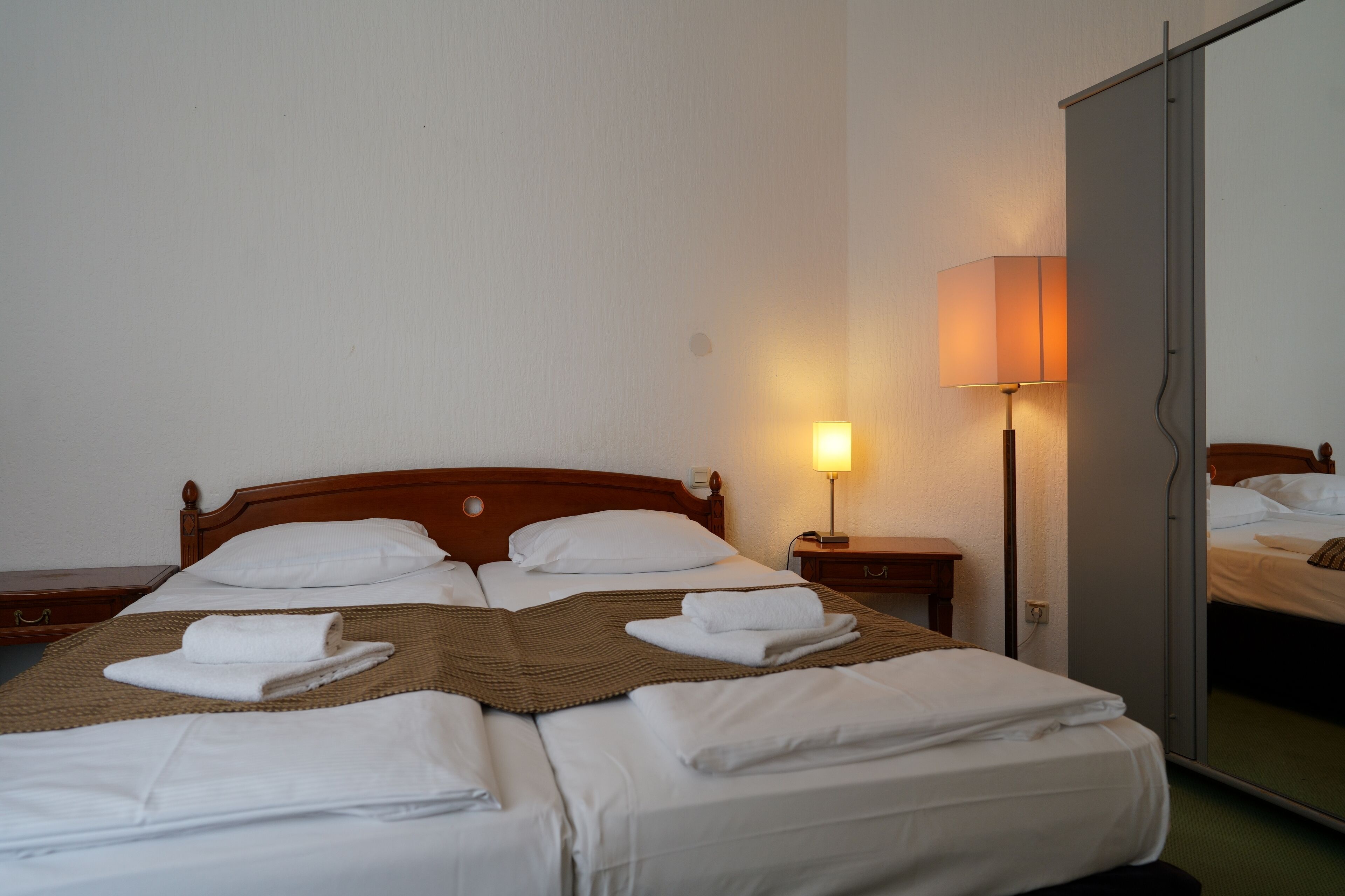 A hotel room with a wooden bed, white linens, a bedside lamp, and a mirror.