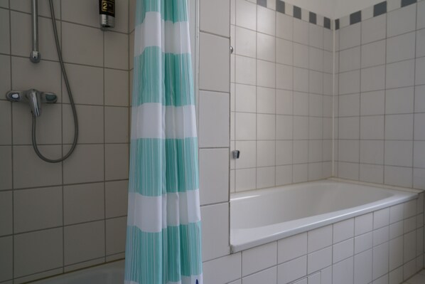 Een badkamer met witte betegelde wanden, een douche met handdouche en een bad.