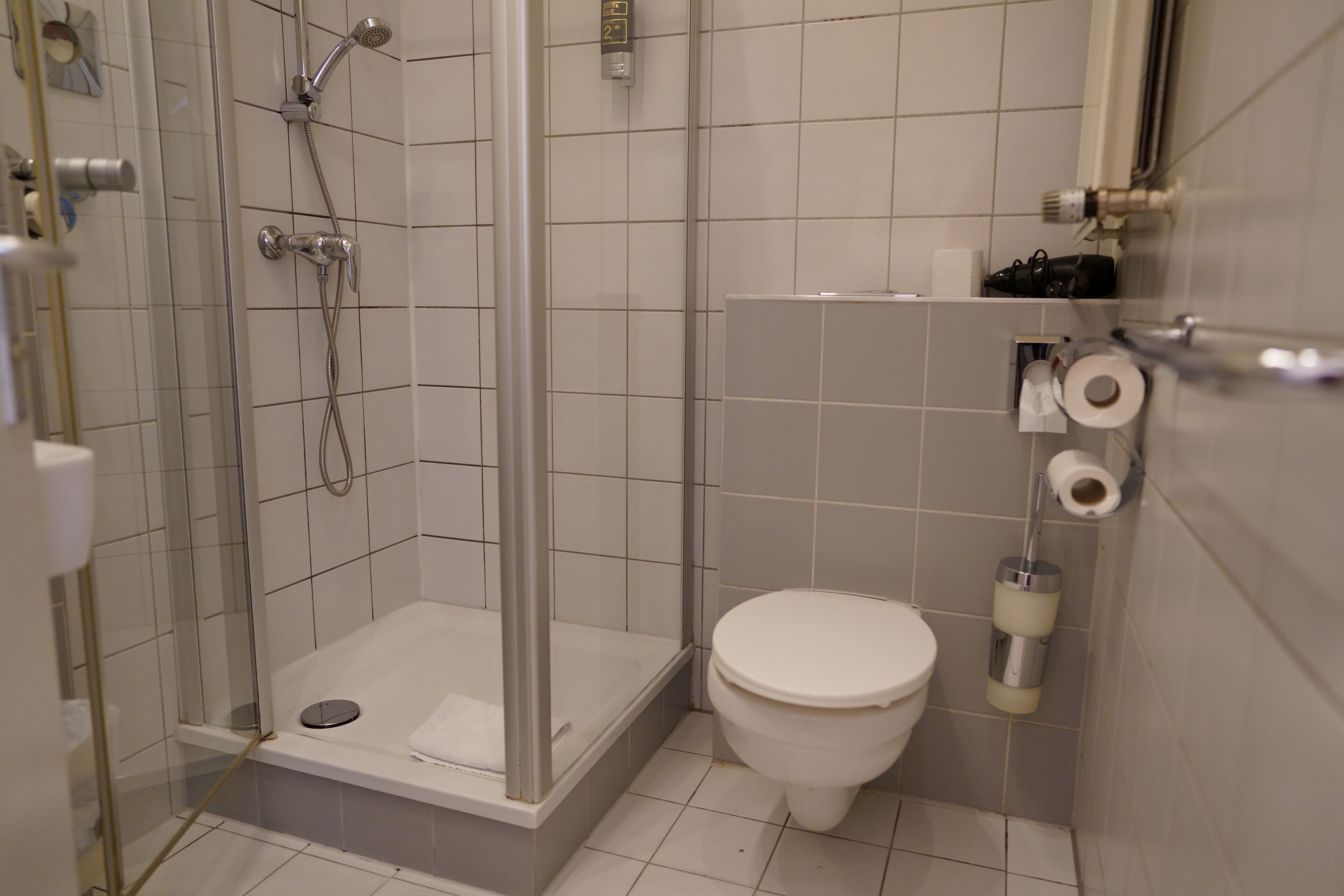 Een moderne badkamer met een douchecabine van glas, een wit toilet en een plank met toiletartikelen.