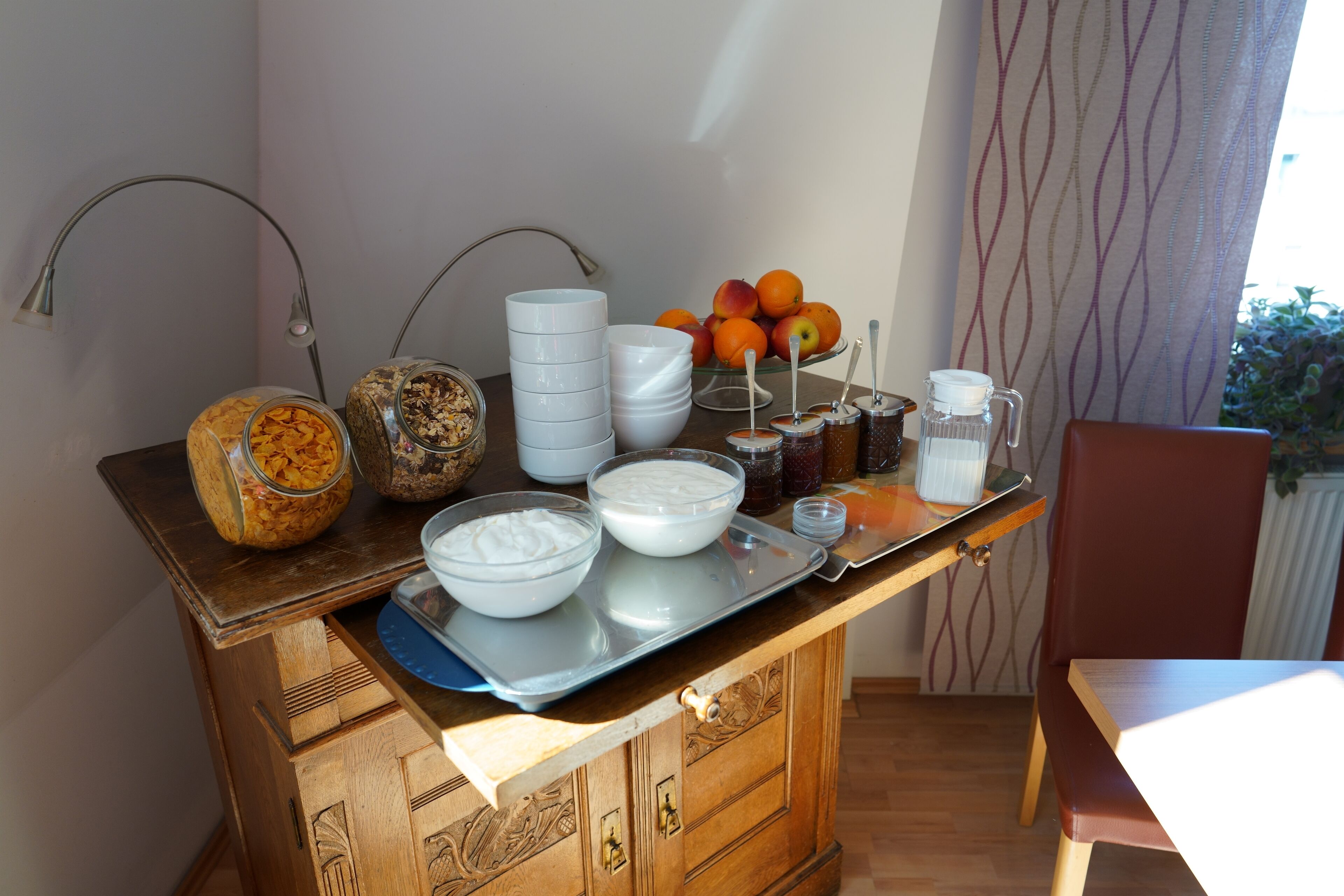 A breakfast bar with various food items, including bowls of yogurt, a fruit bowl, and jars of spreads.