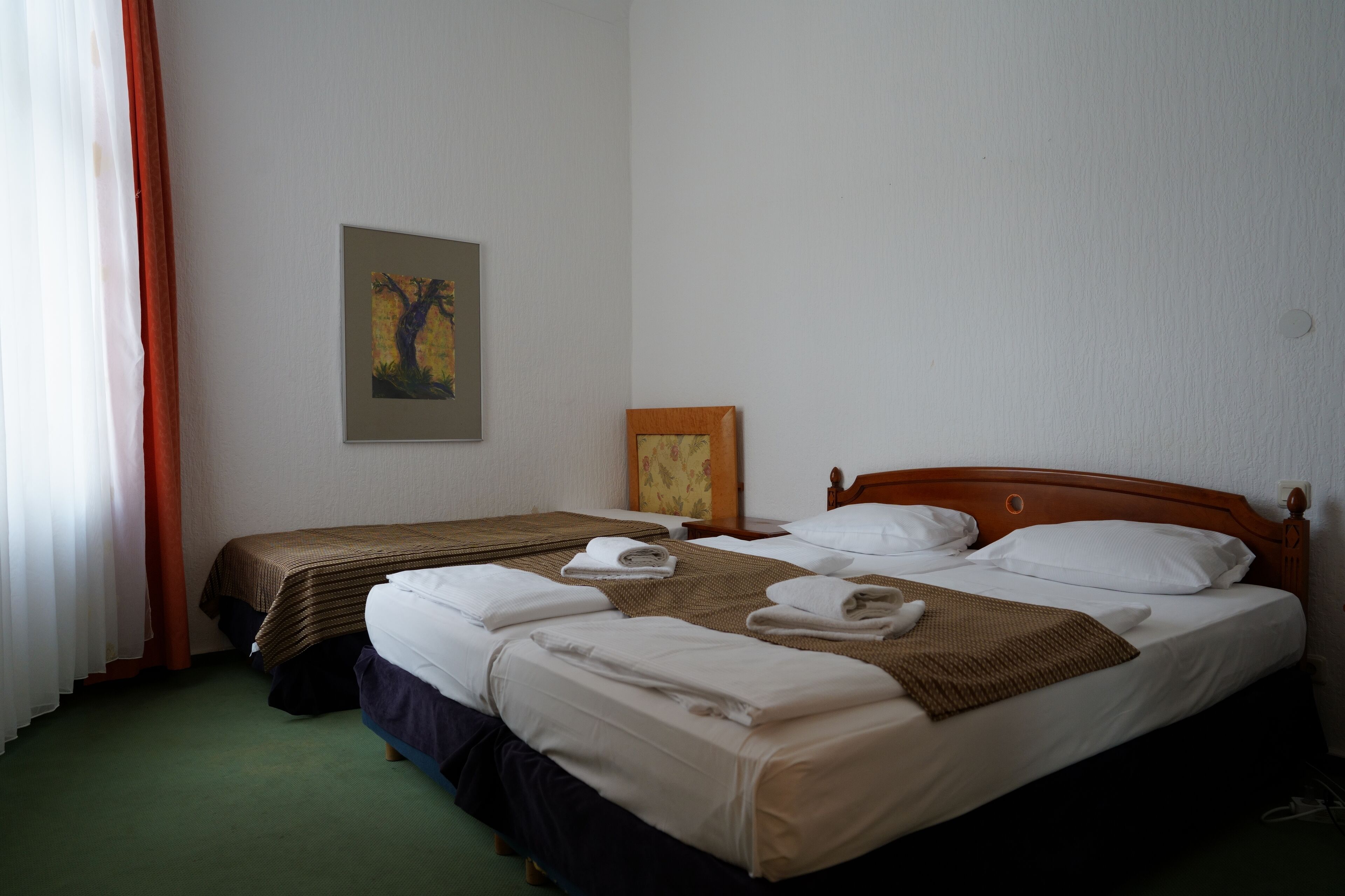 A hotel room with two beds, a wooden headboard, a painting on the wall, and a window with curtains.