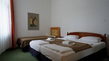 A hotel room with two beds, a wooden headboard, a painting on the wall, and a window with curtains.
