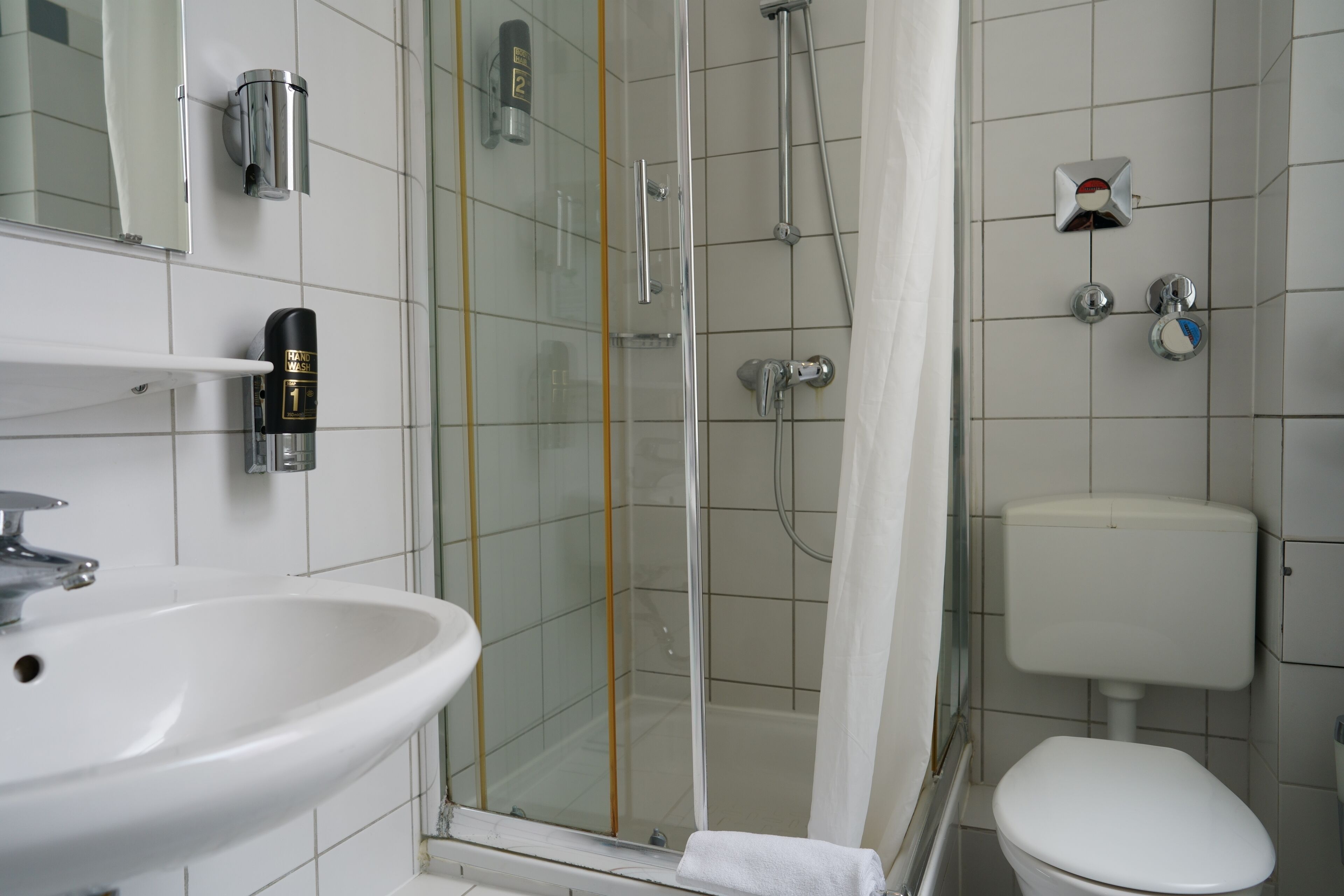 Un baño con lavabo, inodoro, ducha y cabina de ducha con mampara de vidrio.