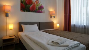 A hotel room with a bed, two bedside lamps, a painting of tulips, and a window with curtains. - Hotel Ambert (Berlin)