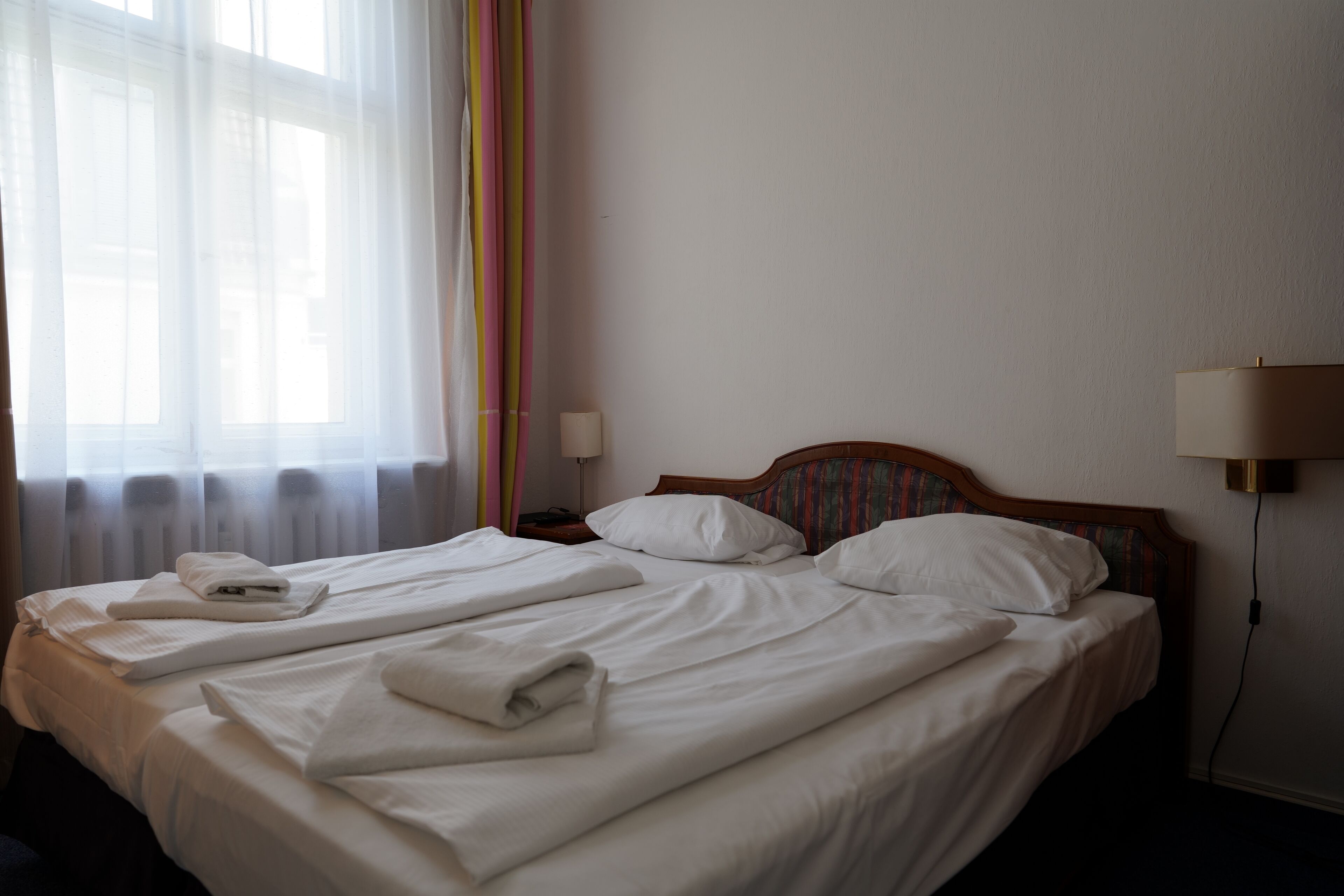 A neatly made bed with white linens, a wooden headboard, and a bedside table with a lamp.