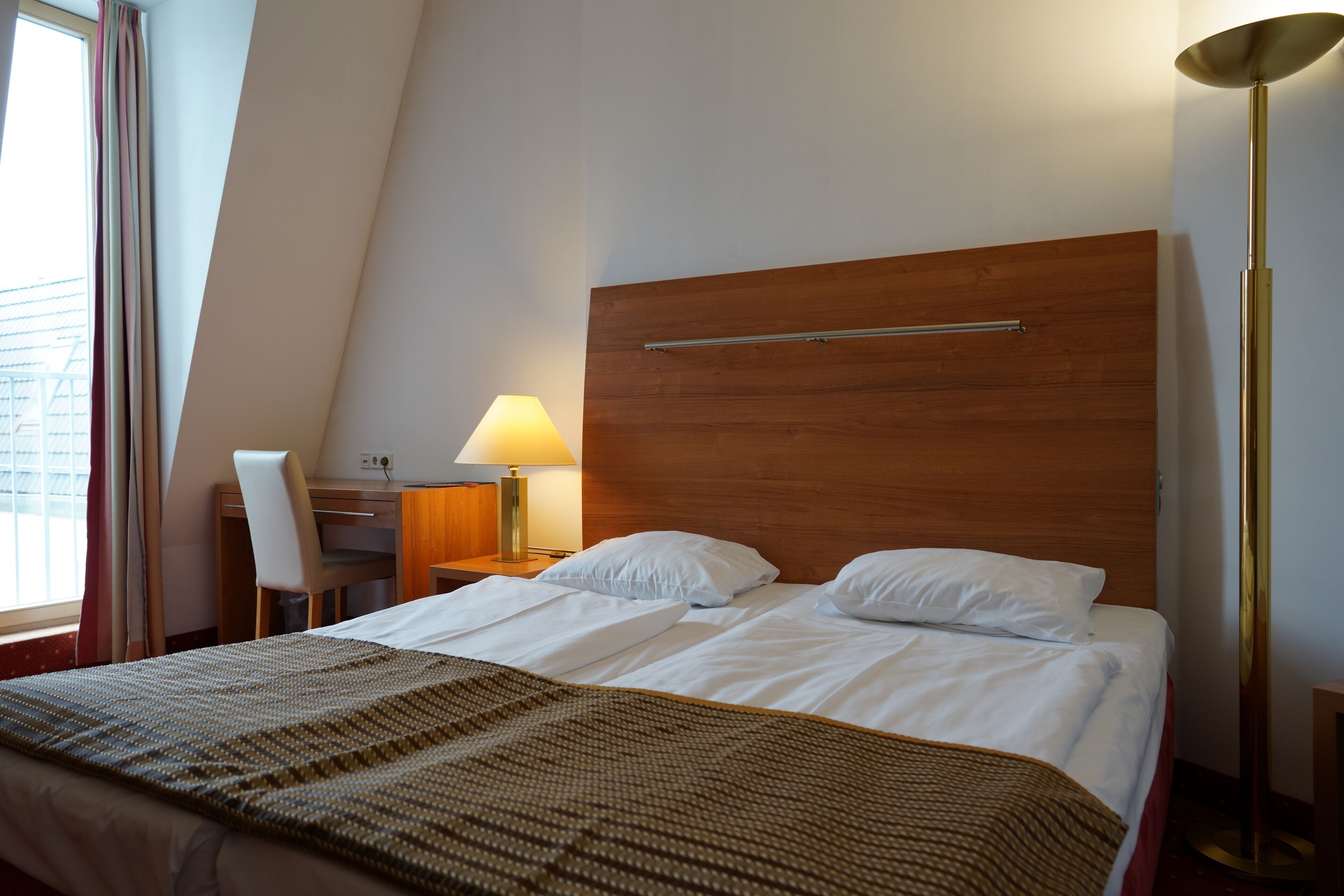 Una habitación de hotel con cama, escritorio, lámpara y lámpara de pie.