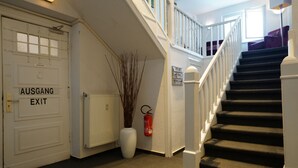 A staircase with a white railing, a white door labeled "AUSGANG EXIT," and a white vase with branches. - Hotel Ambert (Berlin)