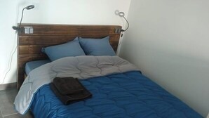 Una cama individual con cabecera de madera, dos almohadas, un edredón azul y una manta marrón doblada.