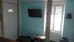 Habitación con paredes verde azulado, un televisor montado, un pequeño banco, una puerta y una ventana con persianas.