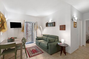 Ein Wohnzimmer mit einem grünen Sofa, einem an der Wand befestigten Fernseher, einem kleinen Tisch mit einer Lampe und einem gemusterten Teppich.