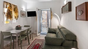 A room with a dining table, chairs, a sofa, a TV, and a door leading to an outdoor area.