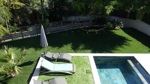 Ein Schwimmbecken mit einer kleinen Liegefläche, umgeben von Rasen und einigen Liegestühlen.