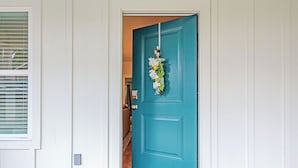 Una puerta verde azulado con decoración floral, un marco blanco y un escalón que da paso a una habitación.