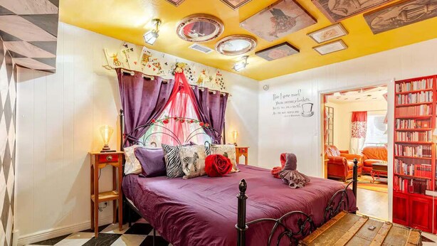A room with a checkered floor, a bed with a purple bedspread, a red rose, and a vintage suitcase. - Hatter House Flagstaff (Flagstaff)