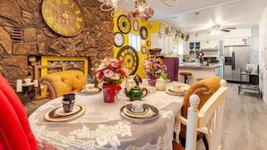 A dining area with a round table set for four, surrounded by chairs. A large wall clock is mounted on the stone wall. - Hatter House Flagstaff (Flagstaff)