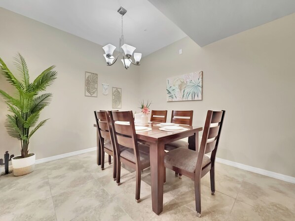 A dining area with a wooden table and chairs, a chandelier, and wall art. - Ground Floor 2 BDR With Garage! Heated Comm Pool! (Mesa)
