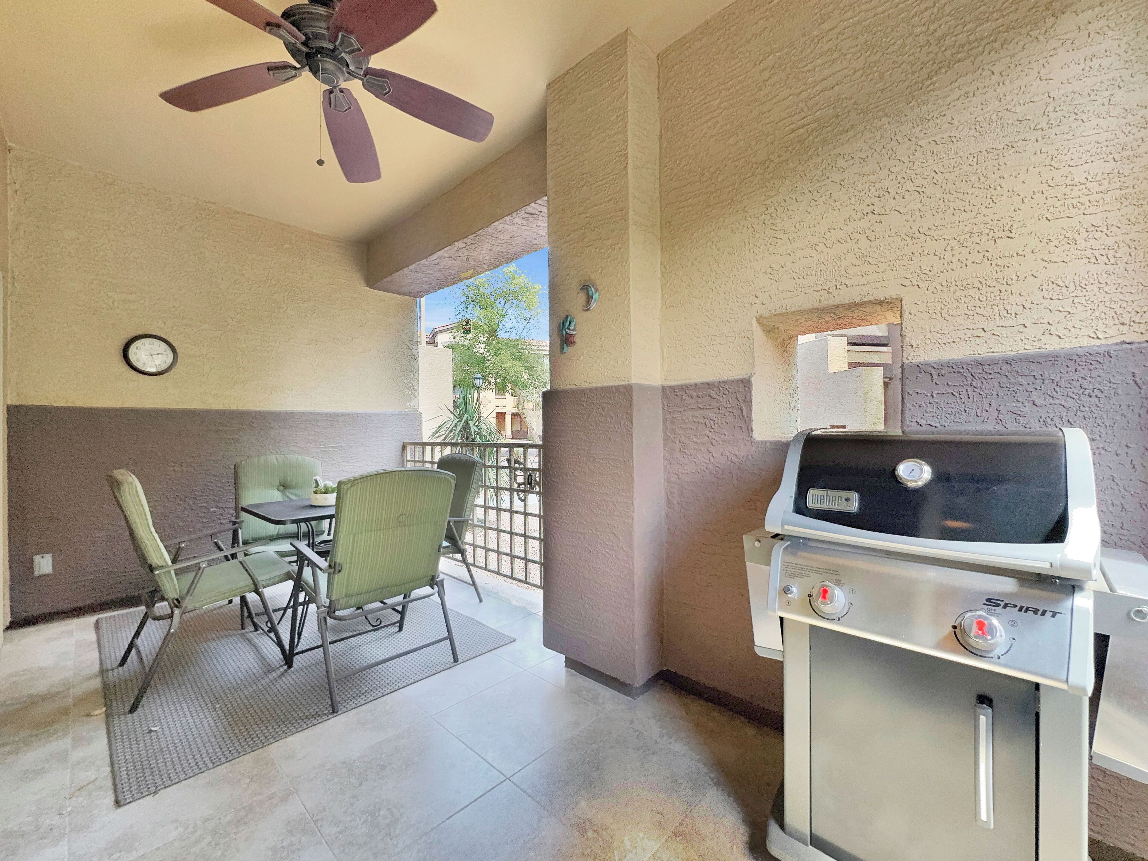 A patio area with a grill, chairs, and a ceiling fan.