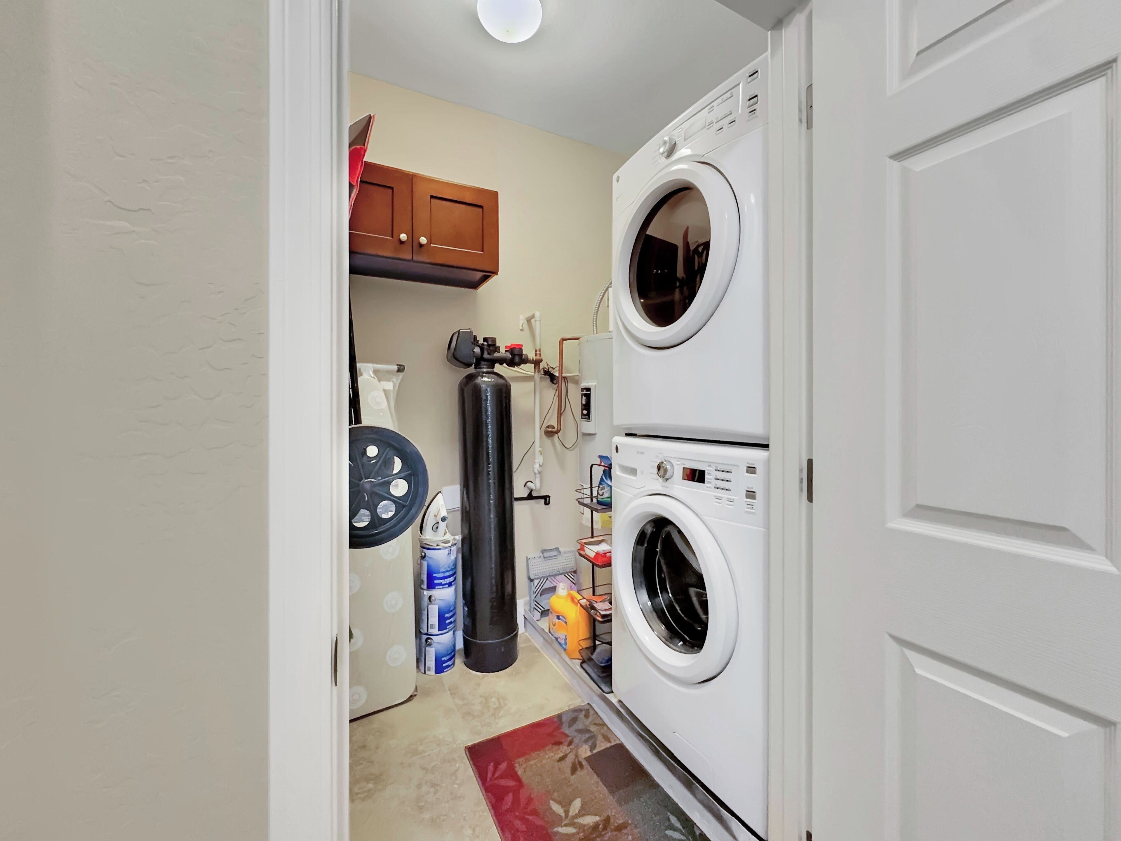 A laundry room with two stacked front-loading washing machines, a water heater, and a hose reel.