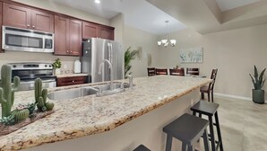 A modern kitchen with granite countertops, stainless steel appliances, and a dining area with a chandelier. - Ground Floor 2 BDR With Garage! Heated Comm Pool! (Mesa)