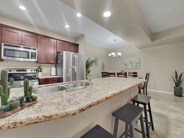 A modern kitchen with granite countertops, stainless steel appliances, and a dining area with a chandelier. - Ground Floor 2 BDR With Garage! Heated Comm Pool! (Mesa)