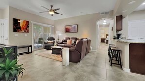A spacious living room with a brown leather sofa, a ceiling fan, and a dining area with bar stools. - Ground Floor 2 BDR With Garage! Heated Comm Pool! (Mesa)