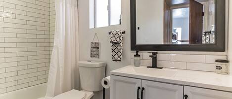 A bathroom with a white toilet, a shower with a white curtain, a large mirror, and a cabinet with black handles.