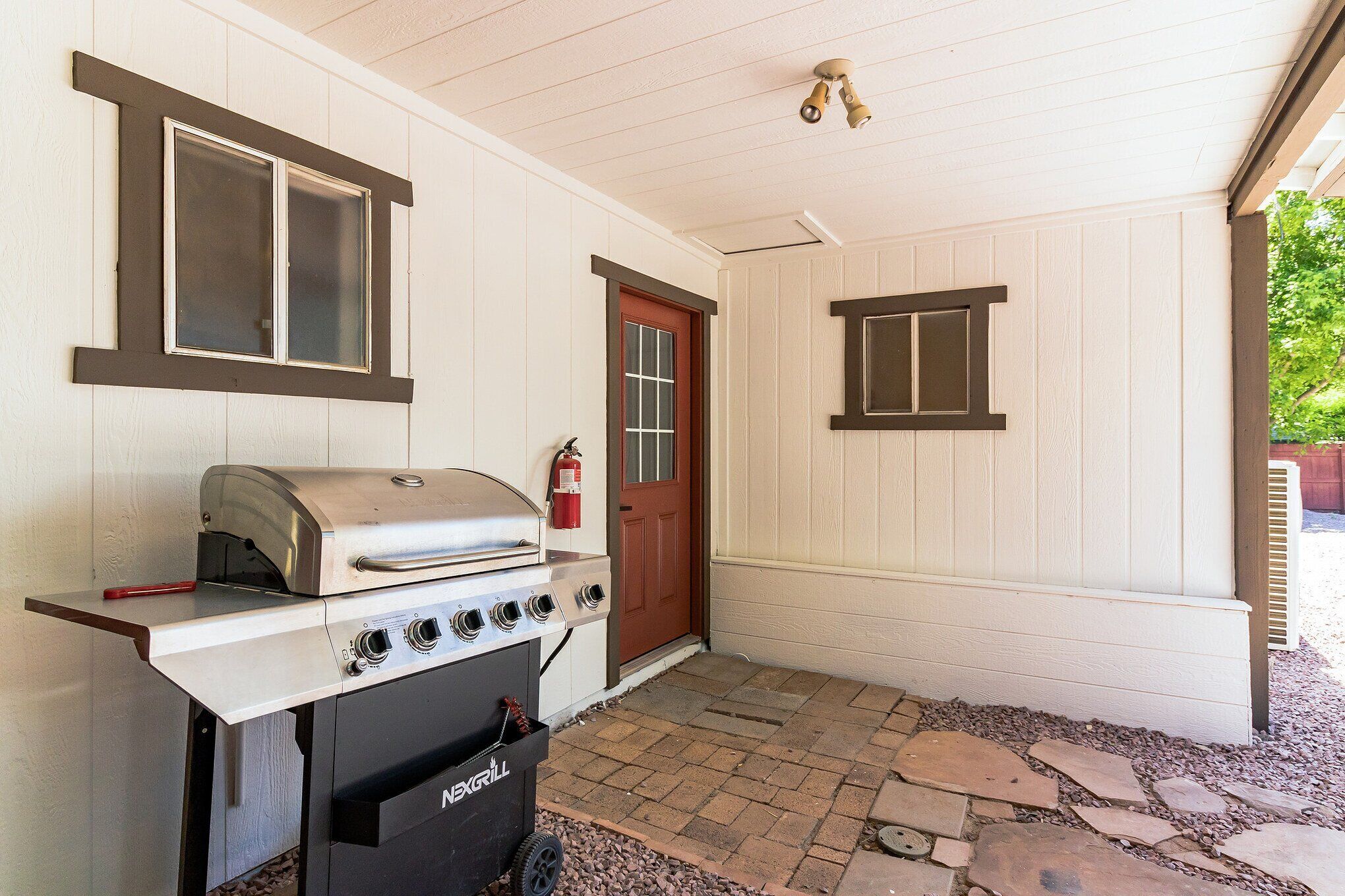 A covered outdoor area with a barbecue grill, a fire extinguisher, and a door.