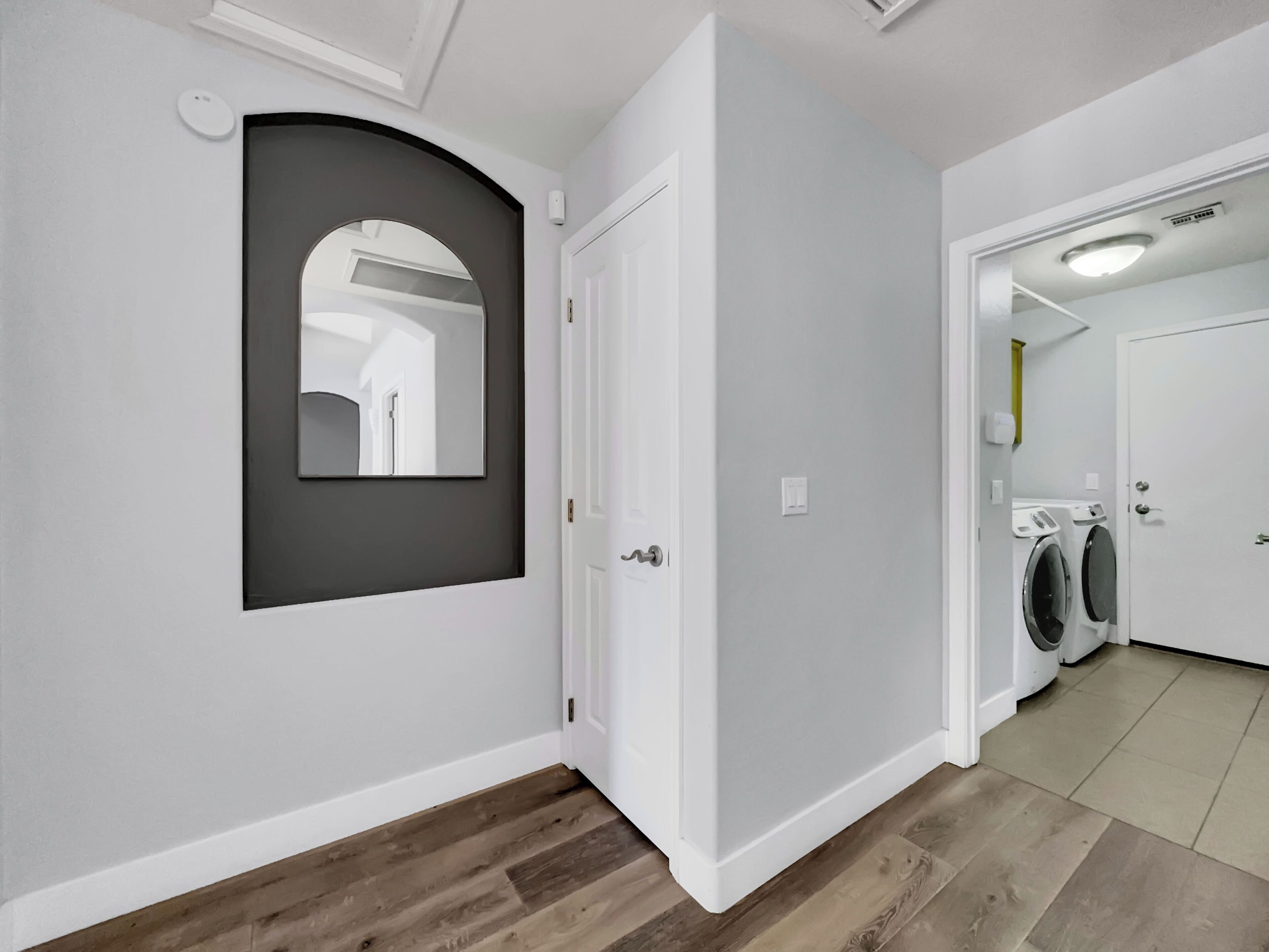 A hallway with a white door, a mirror, and a laundry area with washing machines.