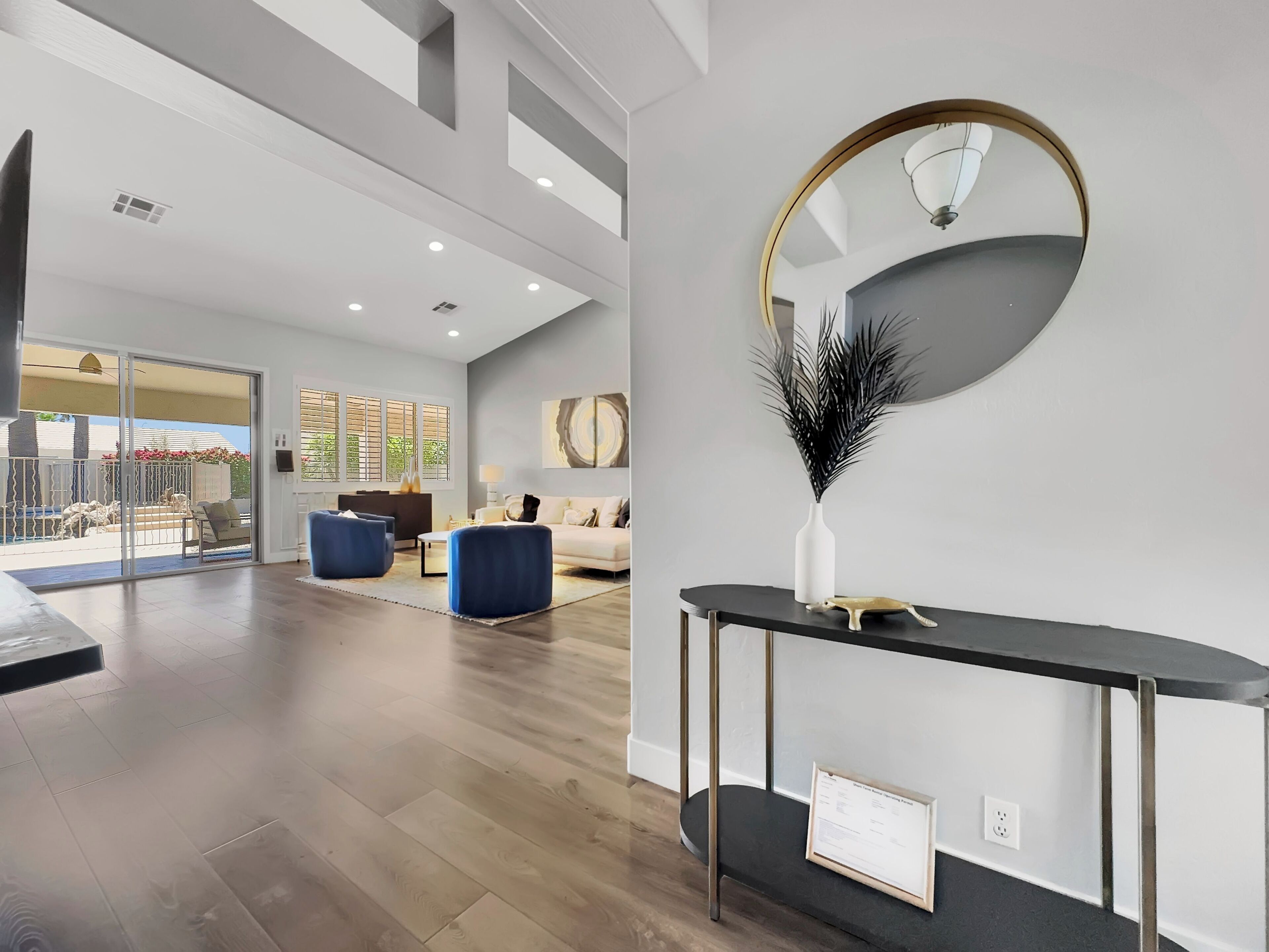A spacious living area with a large window, a round mirror, and a modern console table.