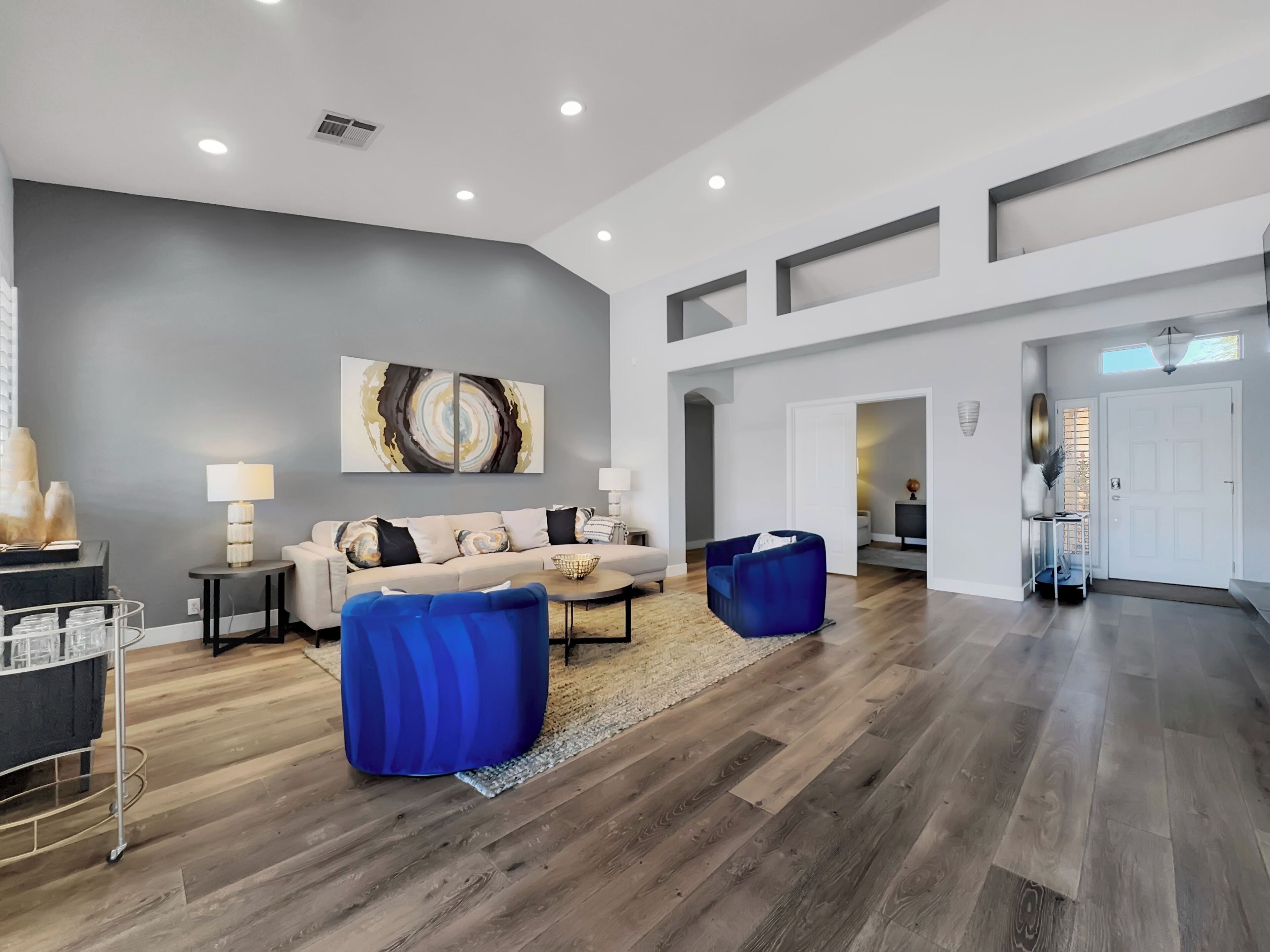 Una sala de estar amplia con una pared de acento gris, un sofá beige y un sillón azul.