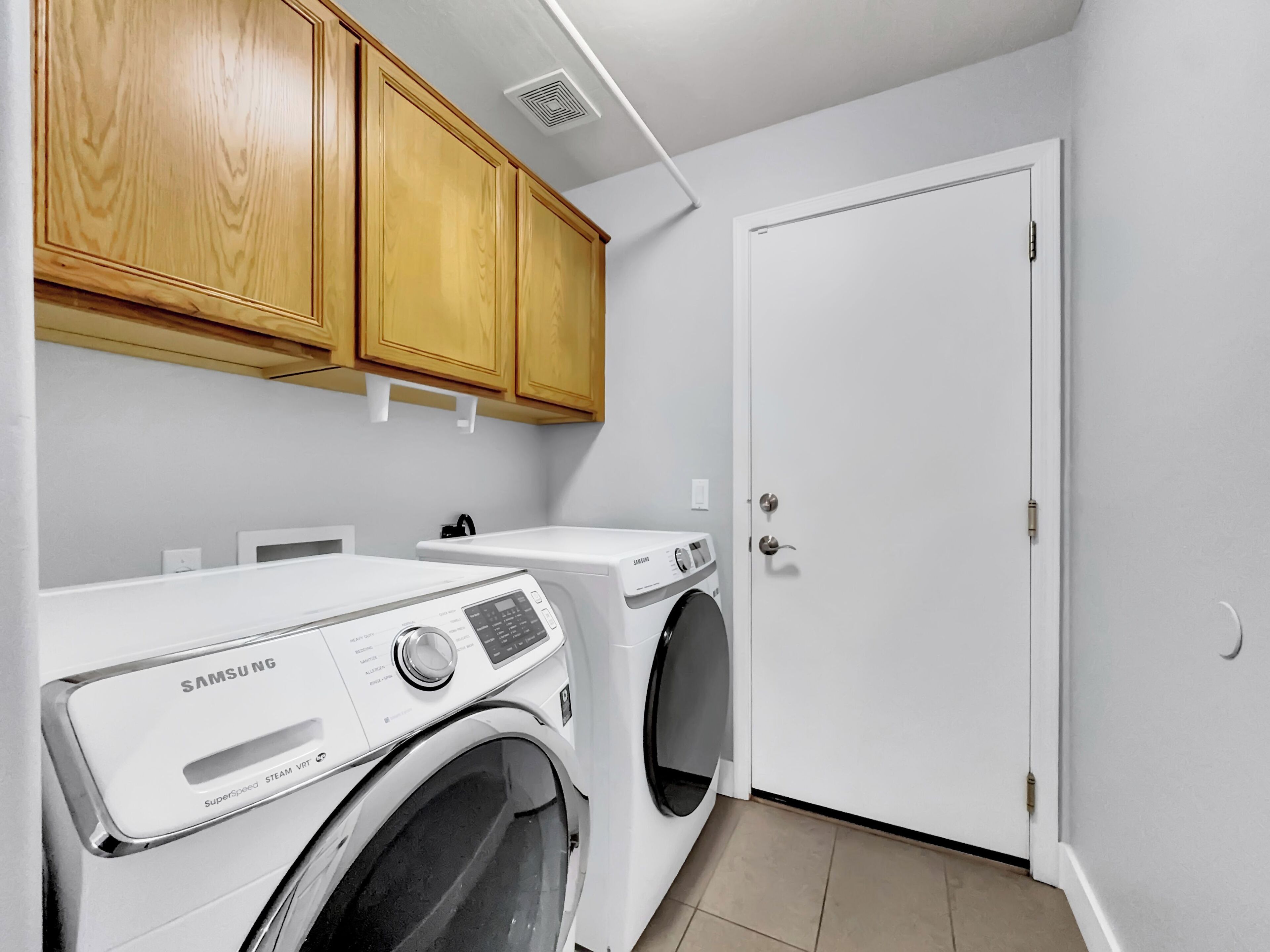 A laundry room with a Samsung SuperSpeed Steam VRt washer and dryer, wooden cabinets, and a white door.