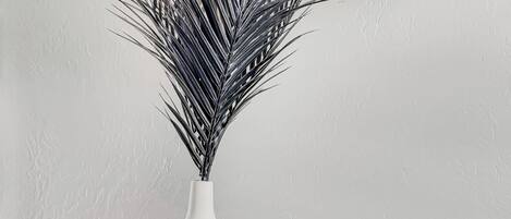 A white vase with a plant on a black table against a textured wall.