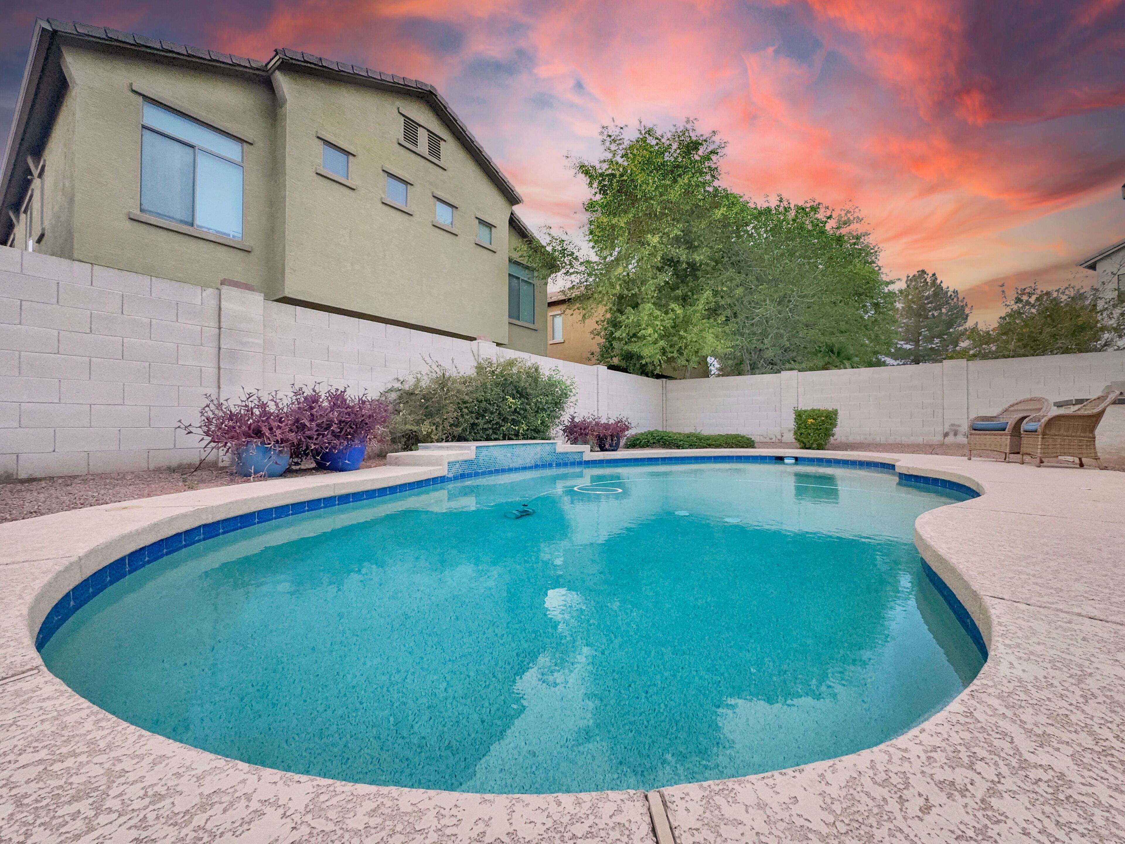 A swimming pool with a curved edge, surrounded by a white brick wall and a house with multiple windows.