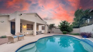 Una piscina de borde curvo, rodeada por un porche cubierto con mobiliario exterior.